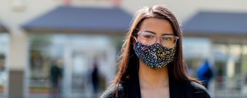 Female Xfinity Retail consultant standing outside in front of Xfinity store wearing face mask